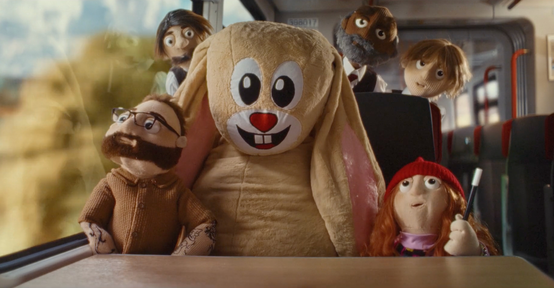 Puppet passengers and a mascot character travelling by train as part of the Woven through Wales brand platform for Transport for Wales.